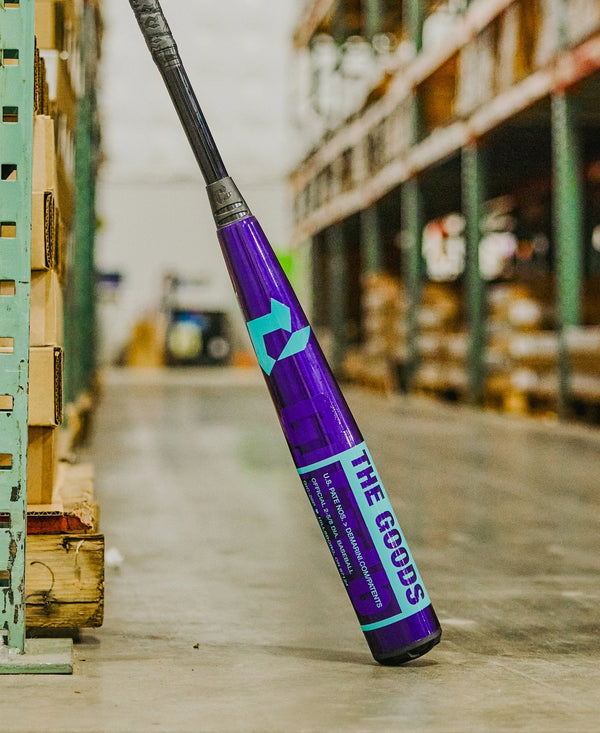 2026 DeMarini The Goods™ Royal Purple -3 BBCOR Baseball Bat leaning against some shelving