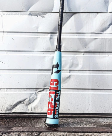 2026 DeMarini The Goods™ -3 BBCOR Baseball Bat leaning against a textured wall