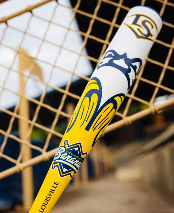 Close-up of the 2025 Louisville Slugger Savannah Bananas Junior Big Barrel -10 USSSA Baseball Bat leaning on a fence