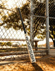 2025 Warstic Bonesaber Hybrid -3 BBCOR Baseball Bat leaning against a ballpark fence